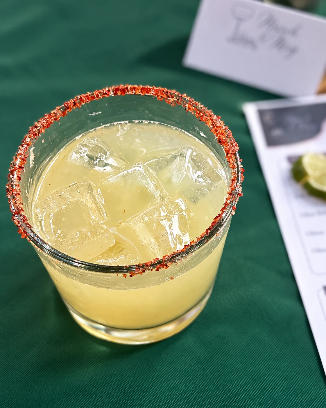 A margarita with a chili-salt rim and class materials softly out of focus behind it