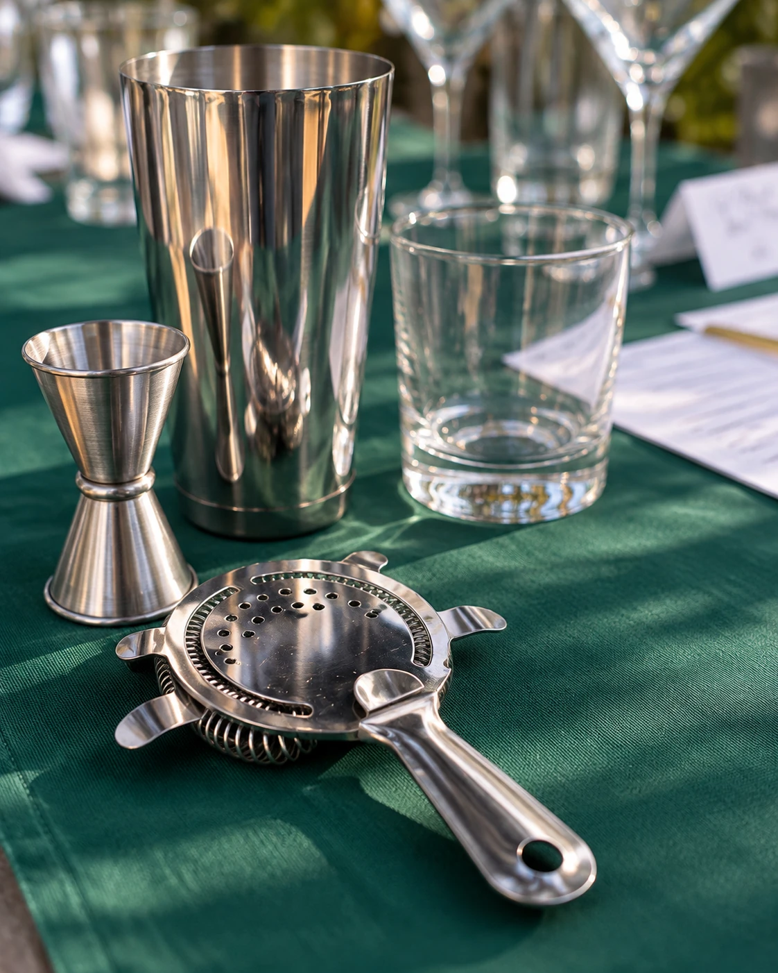 A class station with a strainer, jigger, mixing tin and glassware on a green mat